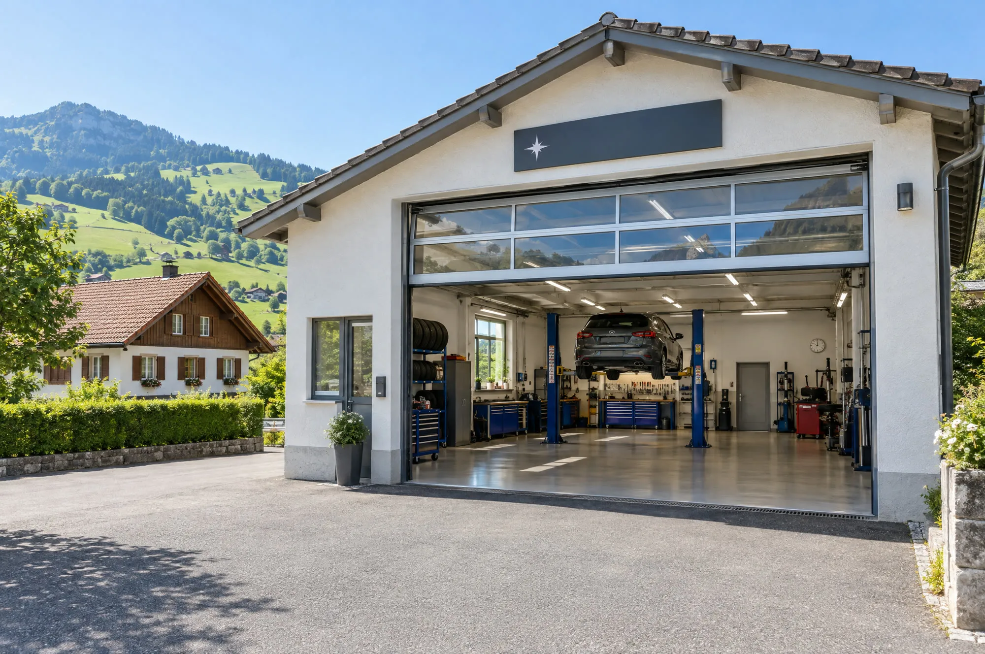 Dorfgarage am sonnigen Morgen: heller Bau mit offenem Glas-Sektionaltor und Blick in die Halle, Vorplatz, Wohnhaus mit Ziegeldach und grüne Hügel dahinter.